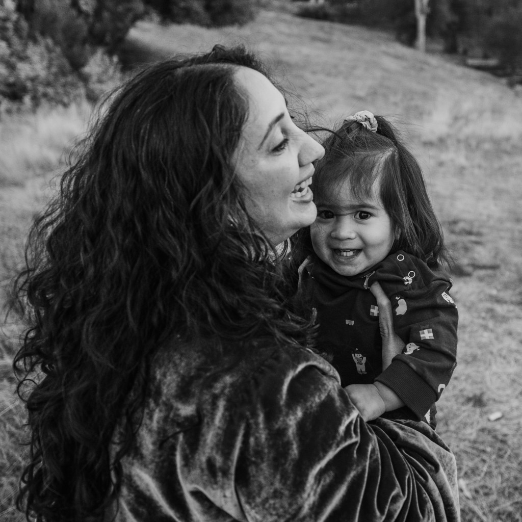 A mother holding her toddler, both smiling and gleefully connected.